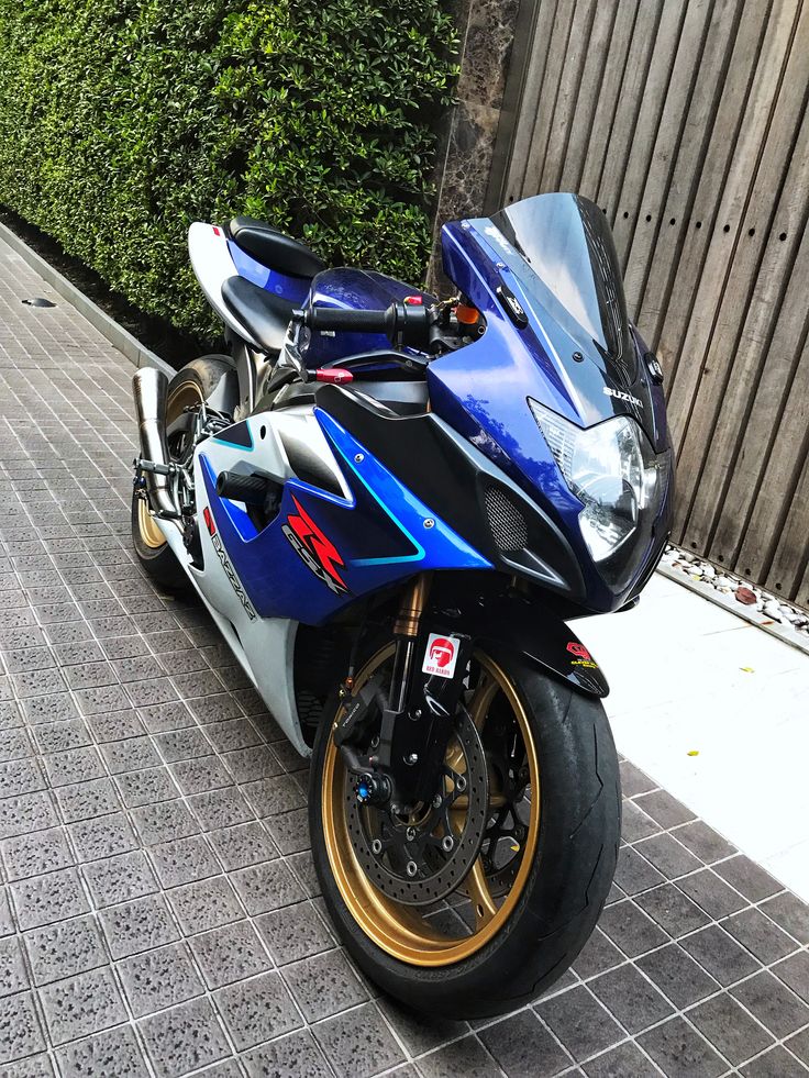 a blue motorcycle parked on the side of a road next to a wooden fence and shrubbery