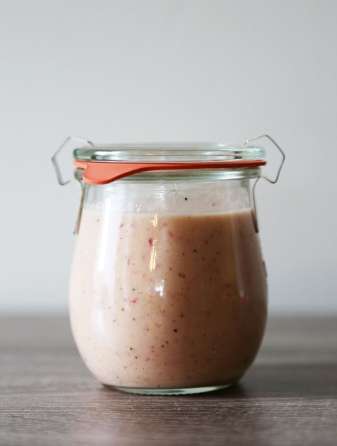 a glass jar filled with food sitting on top of a wooden table next to a red spoon