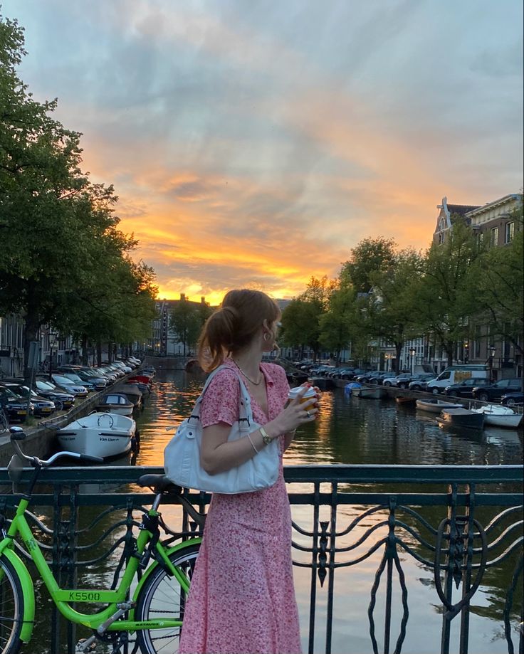 a woman standing next to a green bike near a body of water with boats in the background