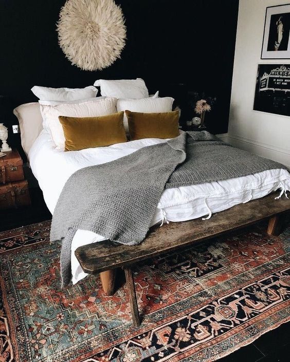 a bed with pillows and blankets on top of it next to a wooden bench in front of a black wall