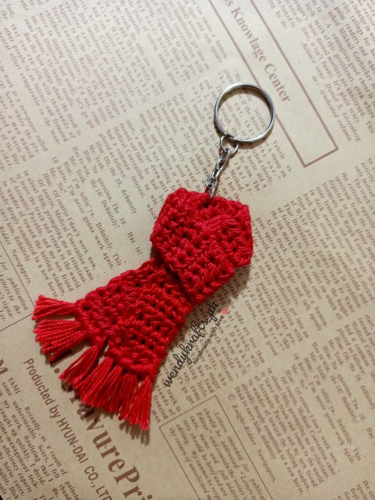 a red knitted scarf keychain sitting on top of an open book,