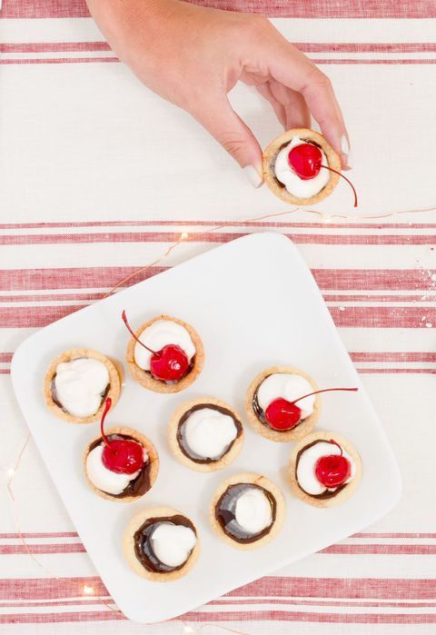 small desserts with cherries and whipped cream are on a white plate next to a person's hand