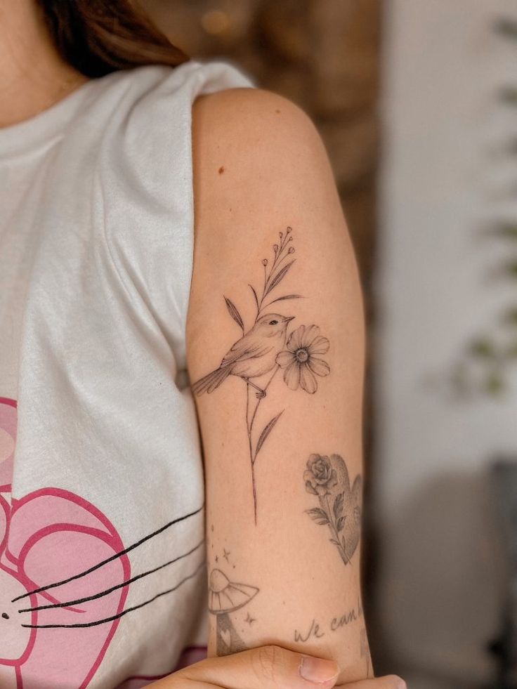 a woman's arm with a bird and flower tattoo on the left side of her arm