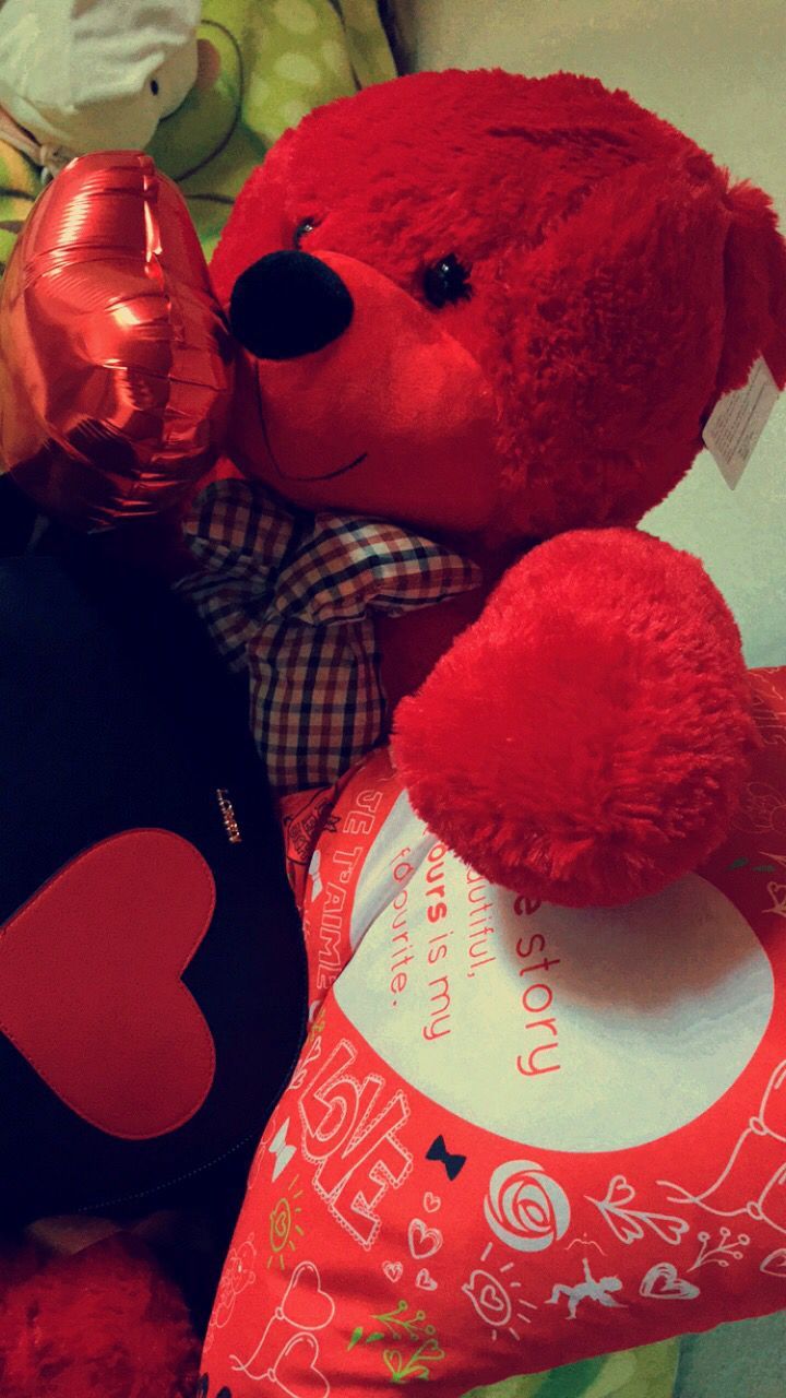 a red teddy bear sitting next to a heart shaped pillow