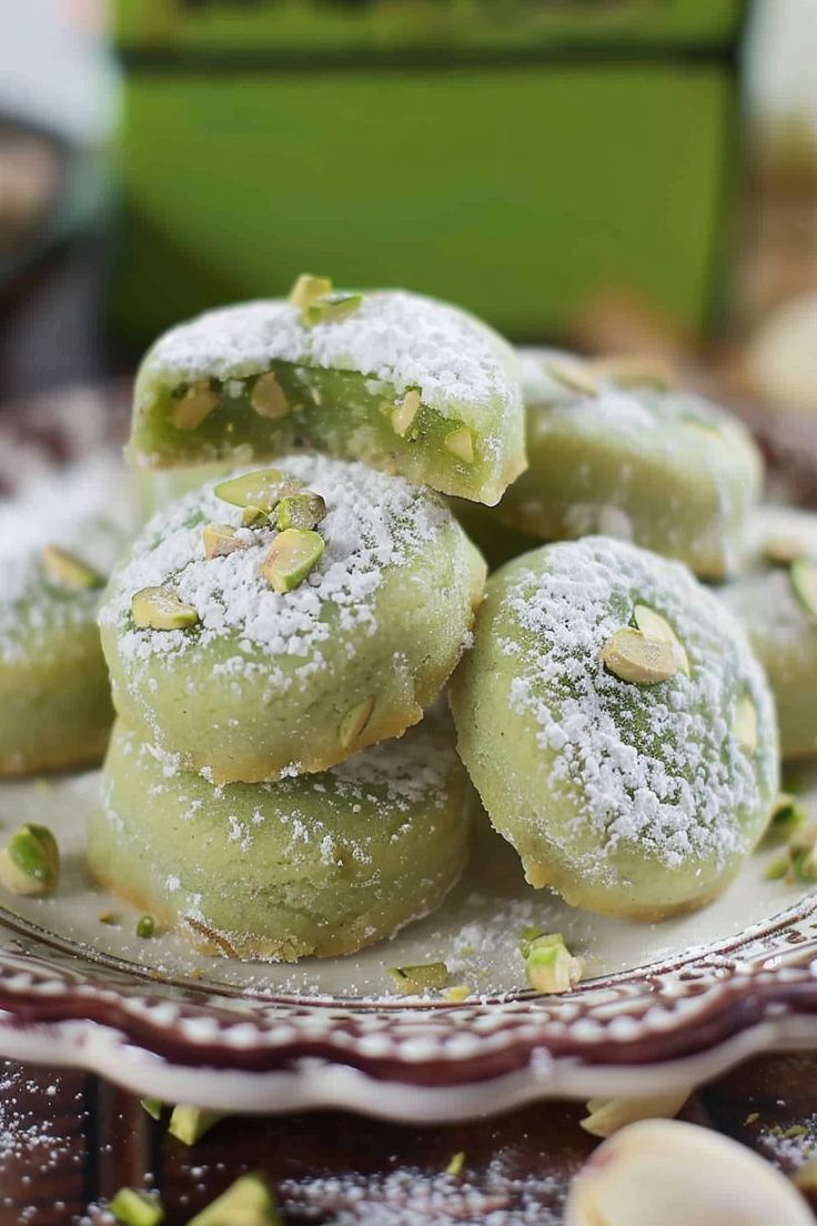 some powdered sugar covered doughnuts on a plate with pistachio sprinkles