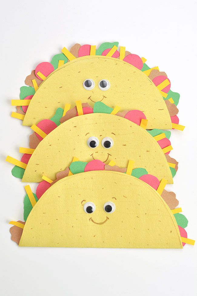 three paper tacos with eyes and hair are on a white surface, one has been cut out to look like a smiling face