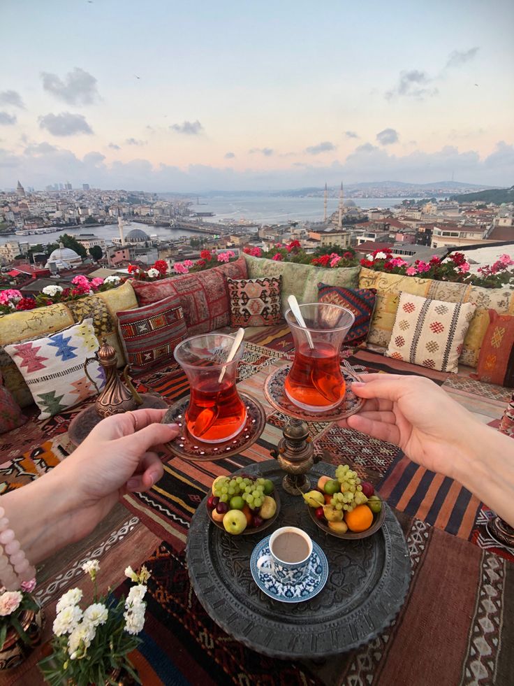 two people toasting with tea and fruit on top of a hill overlooking the city