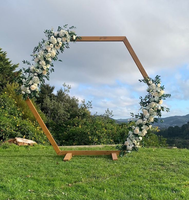 a wooden frame with flowers and greenery on the grass in front of trees,