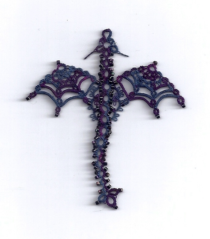 a cross made out of purple beads on a white surface with an intricate design in the middle