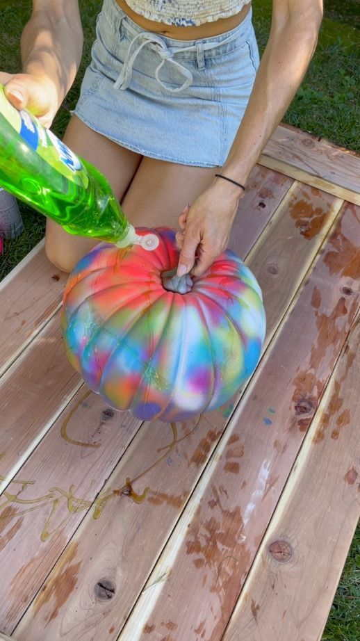 a woman is painting a pumpkin on a picnic table with spray paint and an umbrella