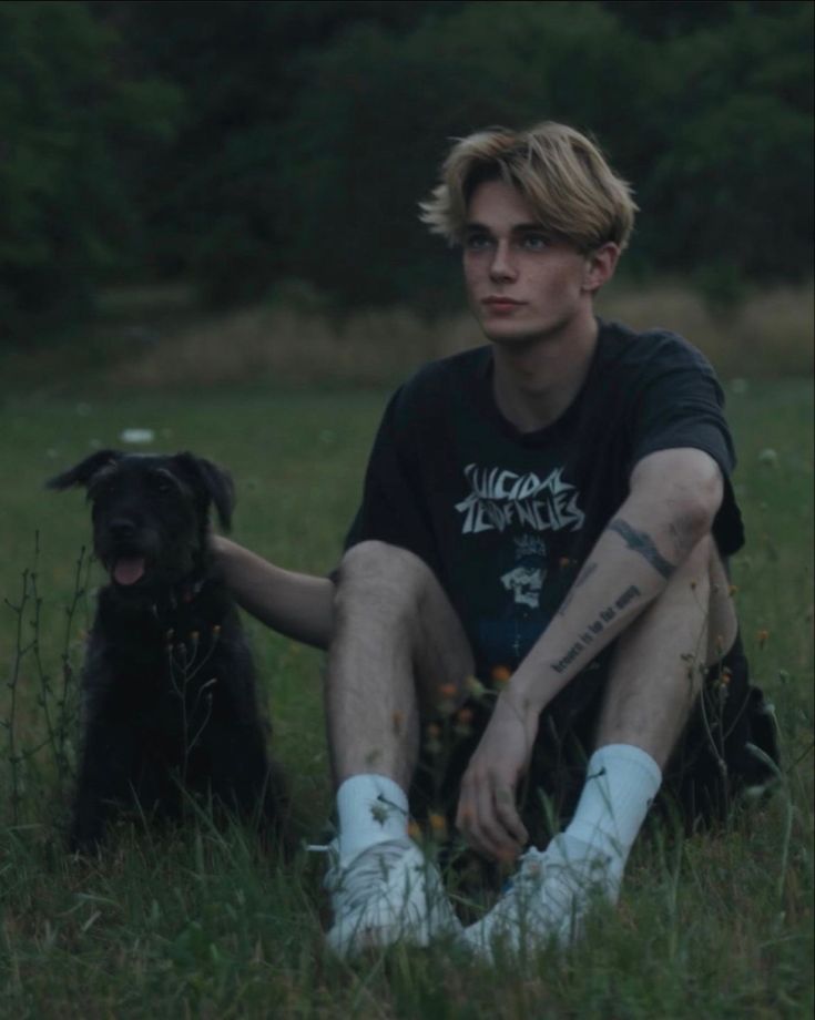 a young man sitting in the grass with his dog