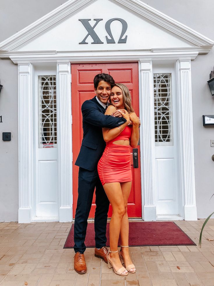 a man and woman standing in front of a red door with their arms around each other