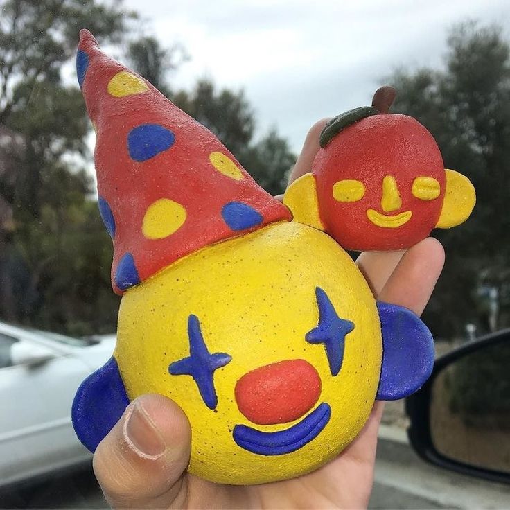 a hand holding a yellow and red clown face rock