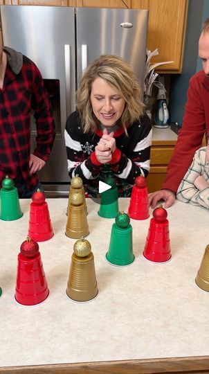 three people standing around a kitchen table with christmas decorations on it and one person pointing at the top