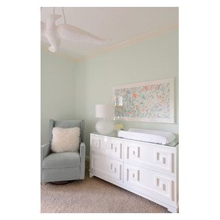 a baby's room with a gray chair, white dresser and painting on the wall