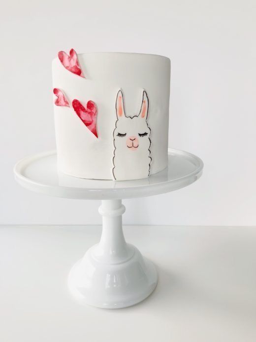 a white cake decorated with an image of a llama and two hearts on it