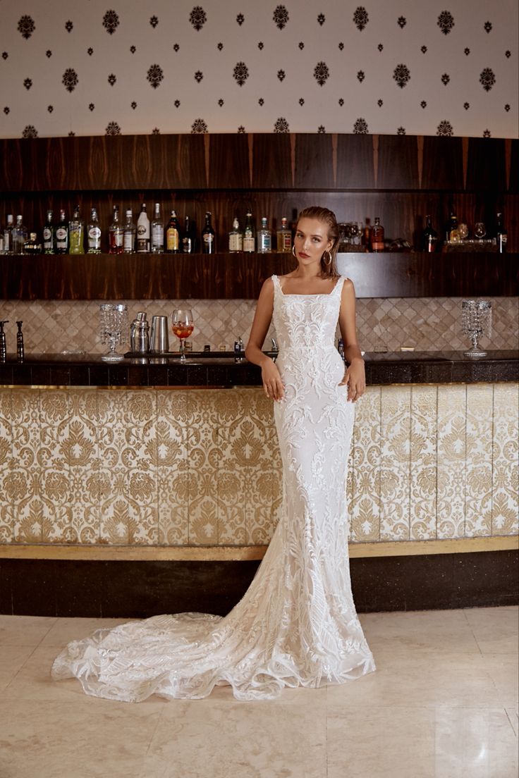 a woman standing in front of a bar wearing a wedding dress with an open back