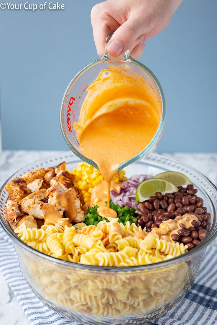 someone pouring dressing into a bowl filled with pasta and veggies, including chicken