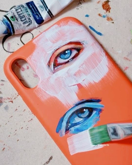 an orange phone case with blue eyes painted on it next to a tube of toothpaste