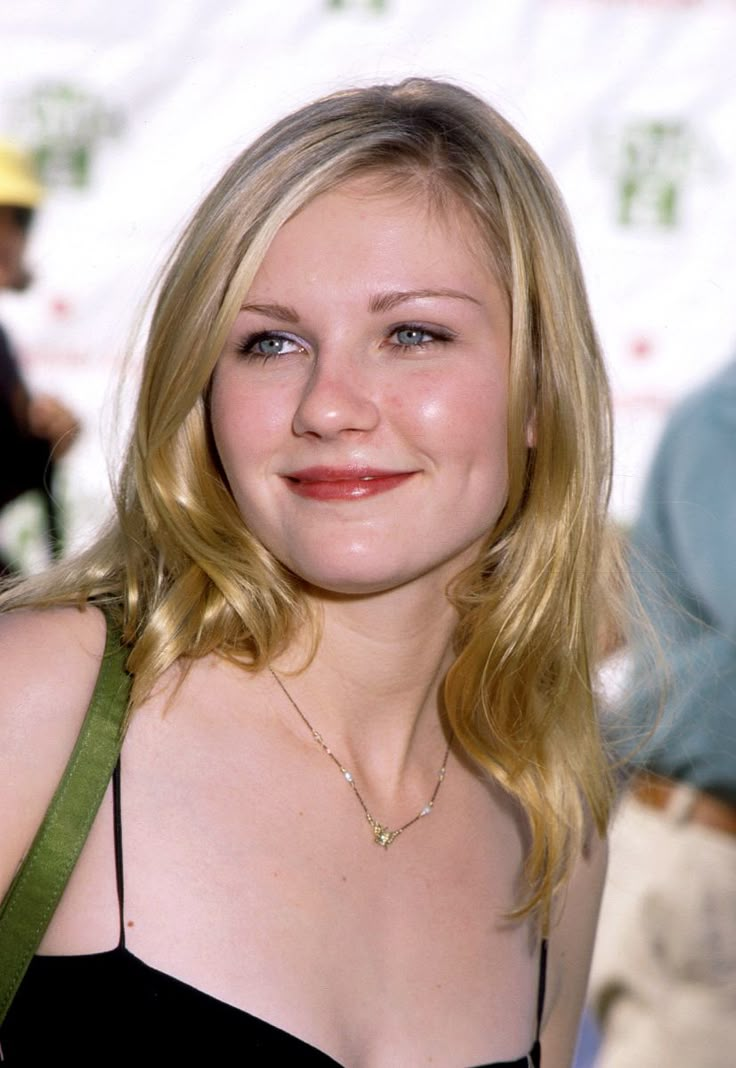 a woman with blonde hair wearing a black top and green strap around her neck smiling at the camera