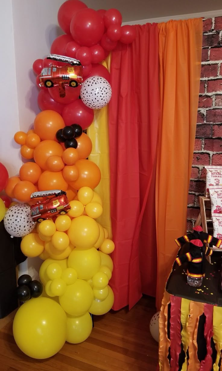 an orange and black birthday party with balloons, streamers, firetrucks and cake