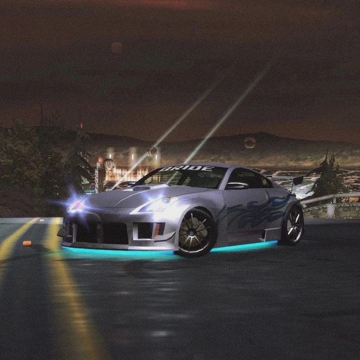 a silver sports car driving down a road at night with bright lights on it's side