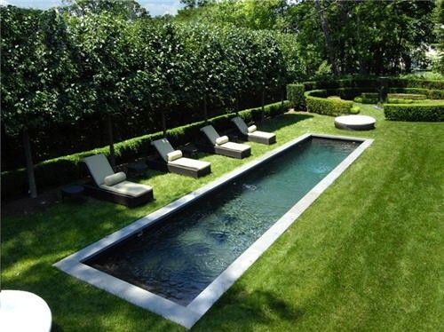 an outdoor swimming pool surrounded by grass and lawn furniture, with lounge chairs around it