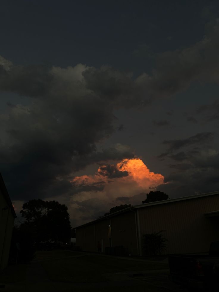 the sky is dark and cloudy at night with clouds in the foreground, some buildings to the right