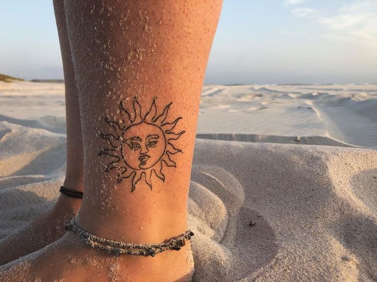 a woman's foot with a sun tattoo on the side of her leg in the sand