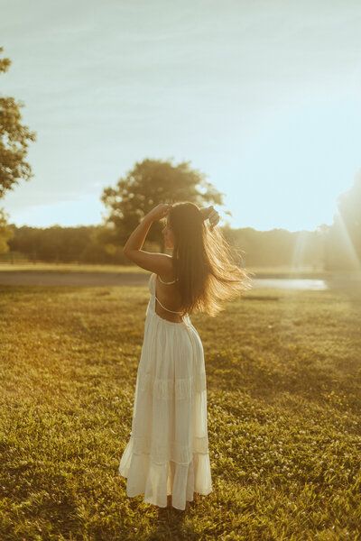 a woman standing in the grass with her back to the camera, looking at the sun