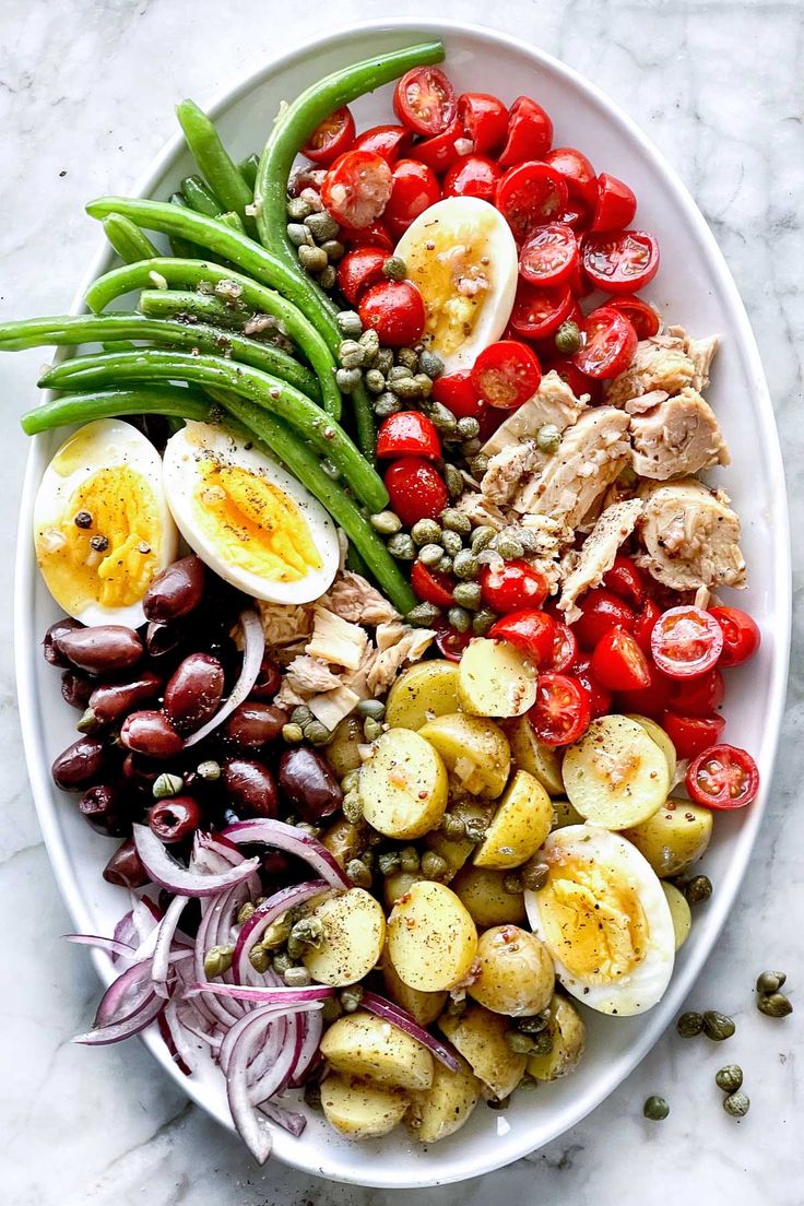 a white plate topped with eggs, tomatoes, green beans and other foodstuffs