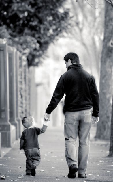 a man holding the hand of a little boy walking down a sidewalk