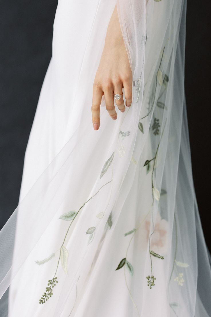 a close up of a person wearing a wedding dress with flowers on it and a veil over their head