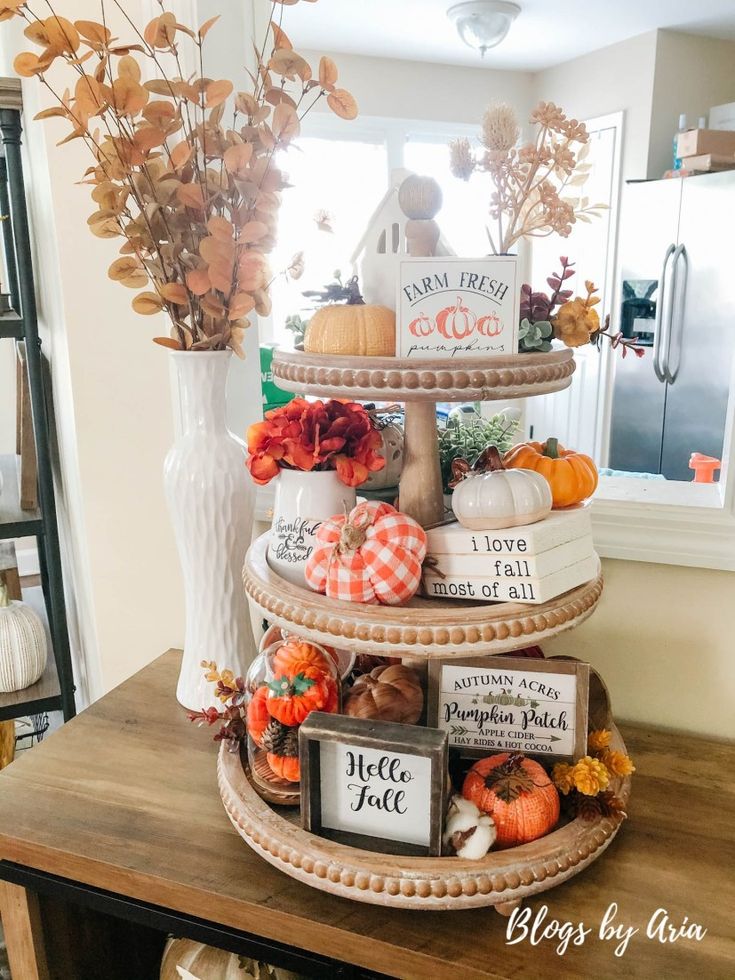 a three tiered tray filled with pumpkins and gourds on top of a wooden table