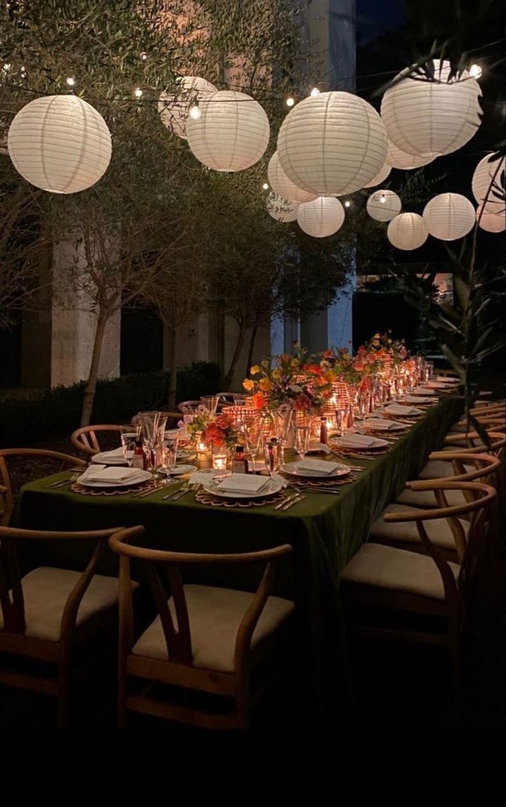 a long table with paper lanterns hanging from it's ceiling and place settings on the tables