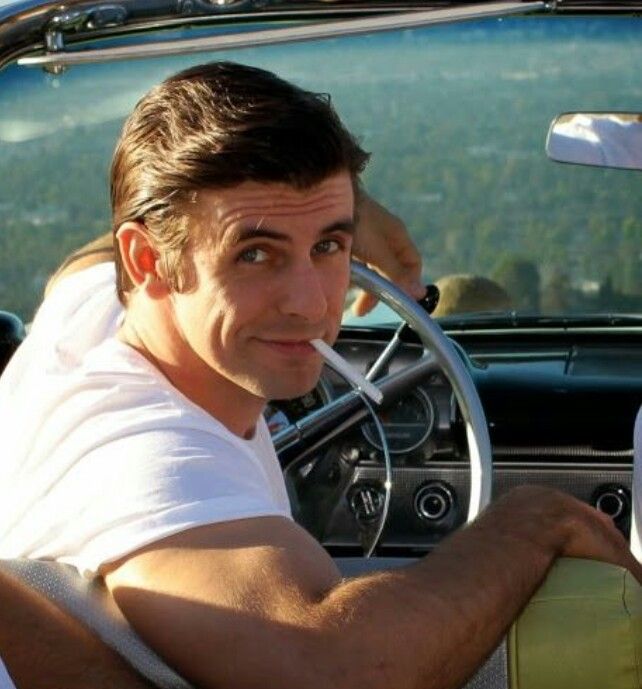 a man sitting in the driver's seat of a classic car looking at the camera