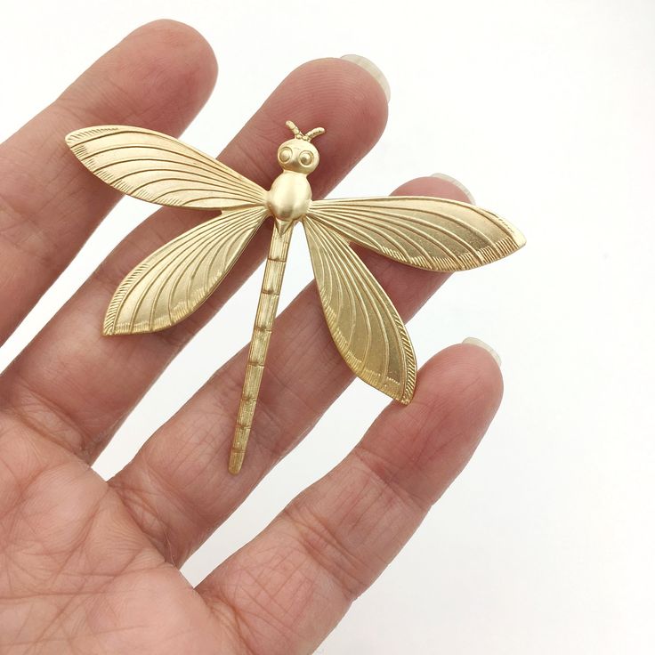 a small gold dragonfly brooch sitting on top of a person's hand