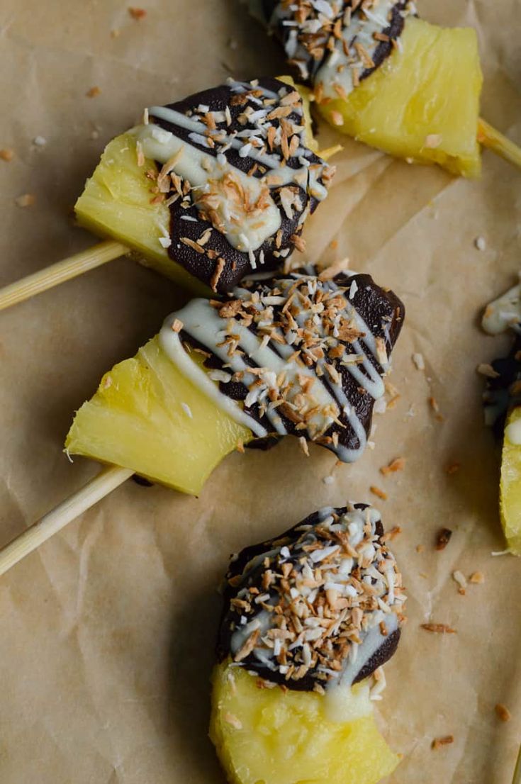 chocolate covered pineapples with coconut sprinkles on a piece of parchment paper