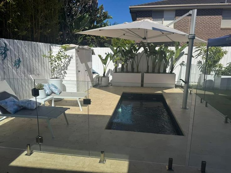 an outdoor pool with chairs and umbrellas next to the fenced in backyard area