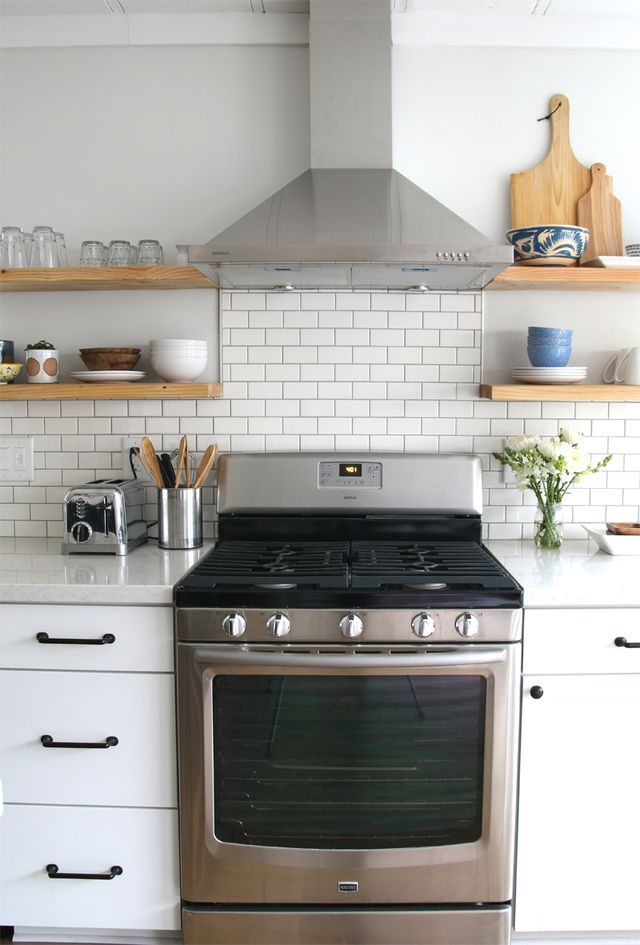 a stove top oven sitting inside of a kitchen next to white cabinets and open shelves