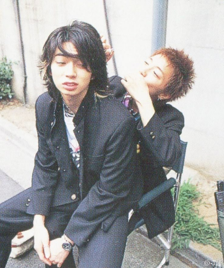 two young men sitting next to each other on top of a chair in front of a building