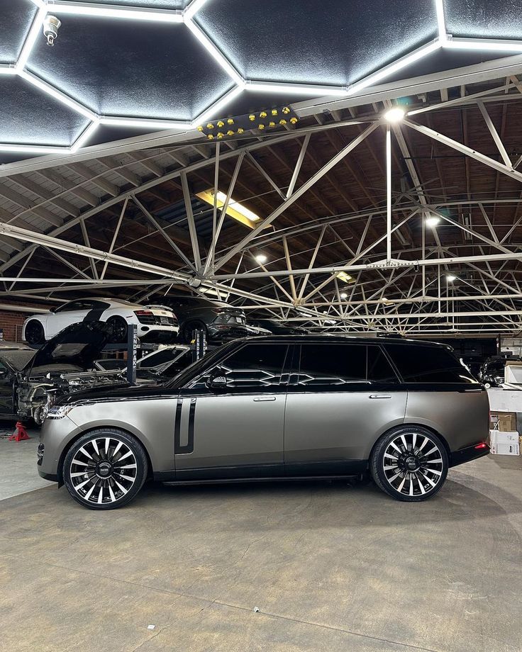 a silver car parked in front of an airplane under a roof covered with metal beams