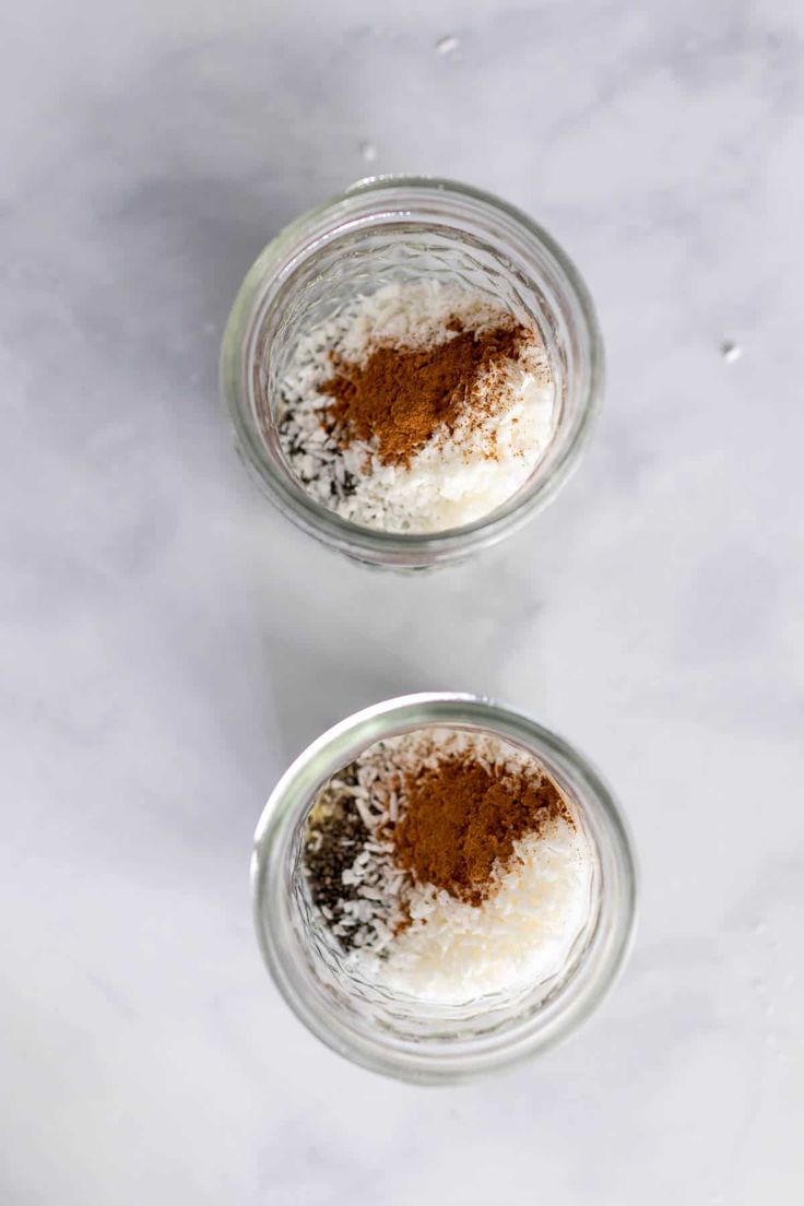 two small glass jars filled with food on top of a white counter next to each other