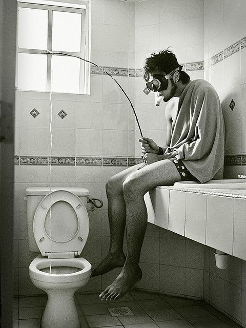 a man sitting on the edge of a toilet in a bathroom with words above him