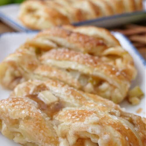 three pastries sitting on top of a white plate next to an apple and cinnamon roll