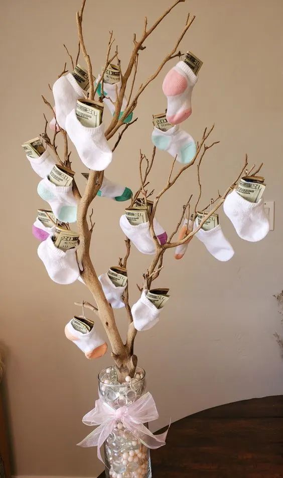 a vase filled with baby's feet and money hanging from a tree branch in front of a wall