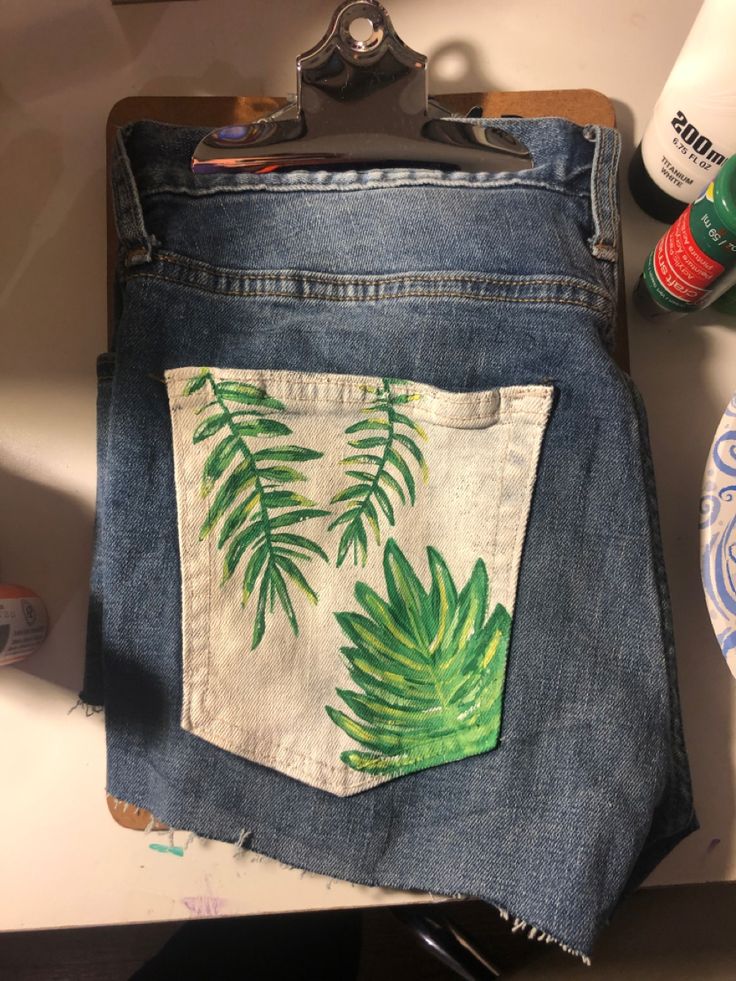 a pair of blue jeans with green leaves painted on the back pocket and inside pockets