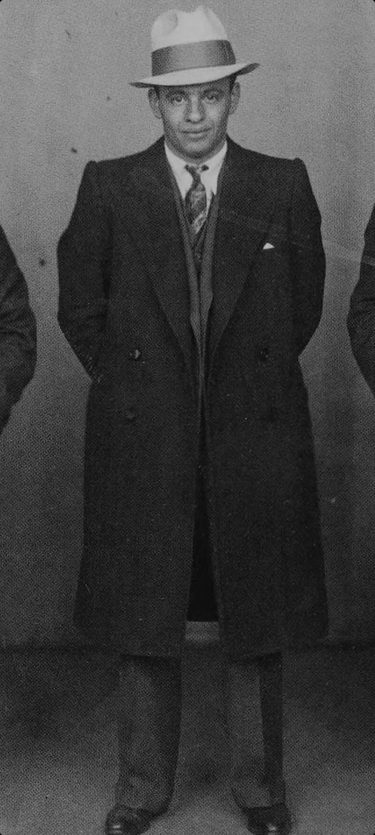 a man in a suit and hat standing with his hands on his hips, looking at the camera