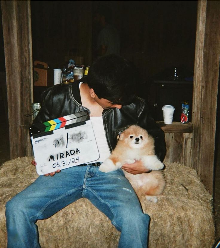 a man sitting on top of a hay bale holding a small brown and white dog