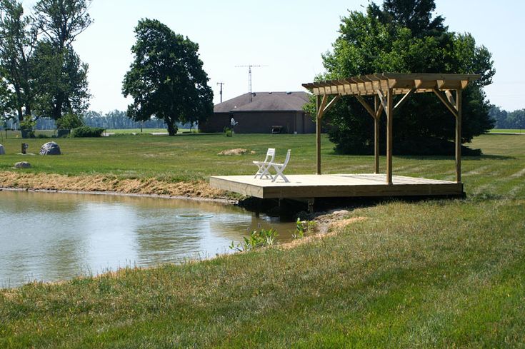 a gazebo sitting on top of a grass covered field next to a lake and picnic area